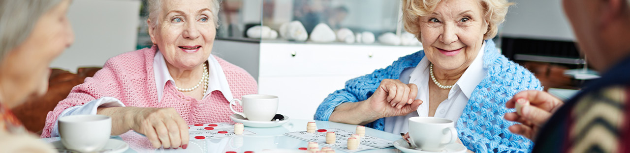 Fröhliche Seniorinnen sitzen gemeinsam an einem Tisch und spielen Bingo bei Kaffee und Tee.